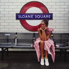 a woman sitting on top of a bench next to a train station sign with the name sloane square