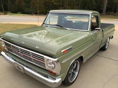 an old green pickup truck parked in a driveway