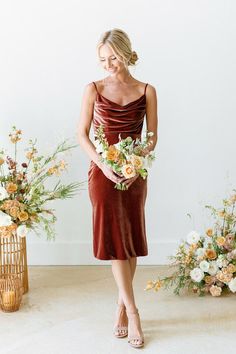 a woman standing in front of some flowers and holding a bouquet with her hands on her hips