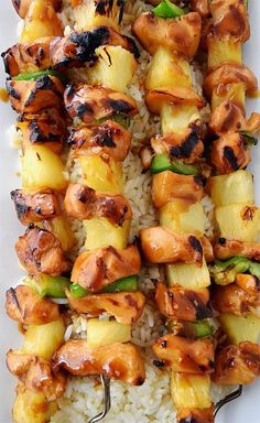 chicken and pineapple skewers with rice on a white platter, ready to be served