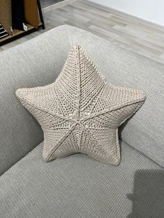 a knitted star pillow sitting on top of a gray couch in a living room