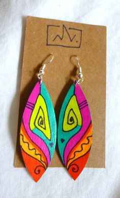 two pairs of colorful wooden earrings on top of a piece of brown paper next to a card