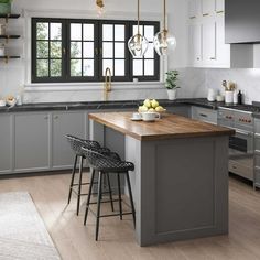 a kitchen with gray cabinets and wooden counter tops, two stools at the island