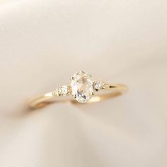 an engagement ring with three stones on it, sitting on a white satin material background