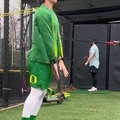 a man in green and white uniform standing on a field with a baseball bat next to him