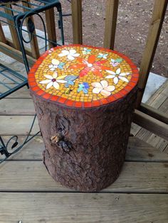 a tree stump with a colorful mosaic design on it's top sitting on a wooden deck