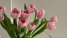 a vase filled with pink tulips sitting on top of a table next to a white wall