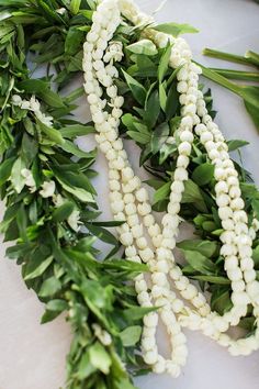 some white beads and green leaves are on a table with flowers in the middle of it