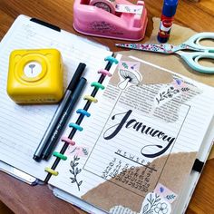 an open planner book sitting on top of a wooden table next to scissors and markers