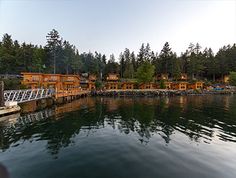 a dock with several wooden cabins on the shore and trees in the backgroud