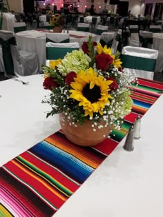 a vase with sunflowers and other flowers sitting on a table in a banquet hall