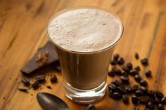 a glass filled with liquid sitting on top of a wooden table next to coffee beans