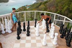 two women playing chess on a balcony overlooking the ocean