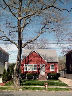 a red house sitting on the side of a road next to a tree and fire hydrant