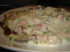 a white plate topped with pasta and meat covered in sauce next to a silver fork