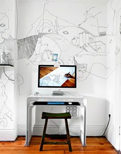 a desk with a computer on top of it in front of a white wall and wooden floor