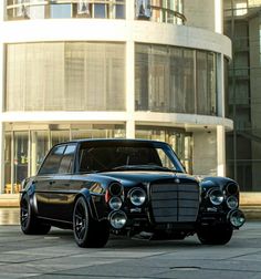 an old black car parked in front of a tall building with a round glass window