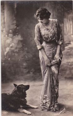 an old black and white photo of a woman standing next to a dog on the ground