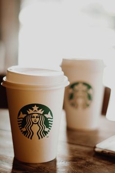 two starbucks cups sitting on top of a wooden table