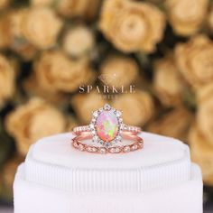 a pink opal and diamond ring sits on top of a white box with roses in the background