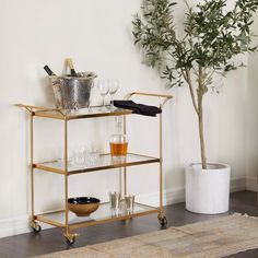 a bar cart with drinks and glasses on it in front of a potted plant