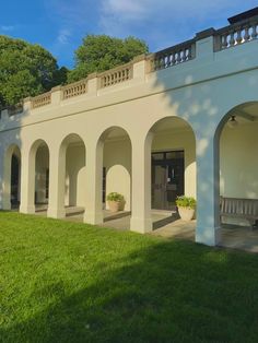 a white building with arches and benches in the grass