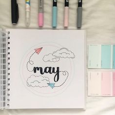 a notebook with the word may written on it next to some markers and pencils