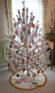 a white christmas tree sitting on top of a table in front of a window filled with ornaments