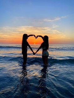 two girls making a heart shape with their hands in the water at sunset or sunrise