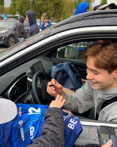 a young man sitting in the driver's seat of a car talking to someone