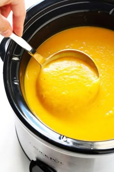 a spoon in a slow cooker filled with yellow liquid and soup or pudding mixture