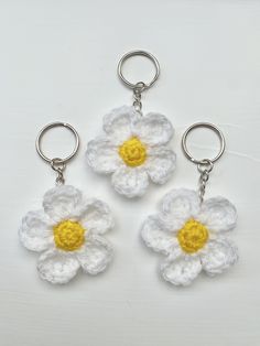 three crocheted white and yellow flower keychains on a white table top