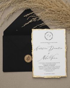 an elegant black and gold wedding suite is displayed on a table with some dried grass