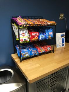 a shelf filled with snacks on top of a wooden counter next to a trash can