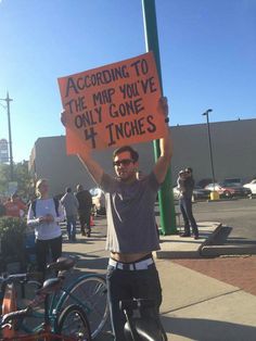 a man holding up a sign that says according to the map you've only gone 4 inches