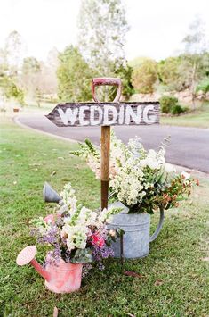 a sign that says wedding on it sitting in the grass next to flowers and watering can