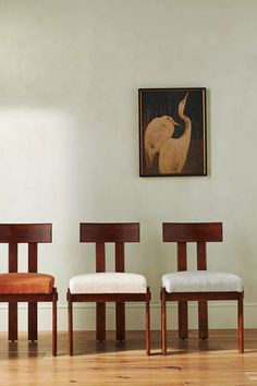 three wooden chairs sitting next to each other on a hard wood floor in front of a painting