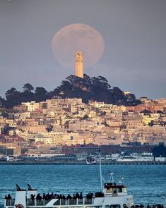 a boat with people on it floating in the water near a large city and a full moon