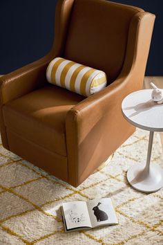 a brown chair sitting on top of a white rug next to a table with a book