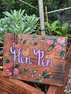 a wooden sign that says the hen pen with flowers and birds on it in front of some plants