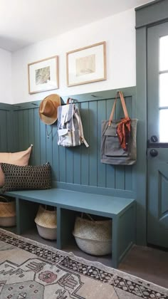 a blue bench with baskets and hats hanging on it's back wall next to a door