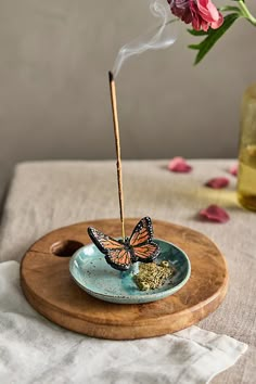 a butterfly incense burner sitting on top of a blue plate next to a pink flower