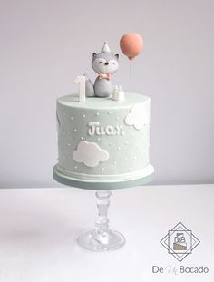 a small cake with a cat on top and two balloons in the air above it