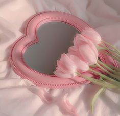 a heart shaped mirror sitting on top of a bed next to pink tulips