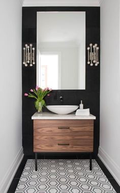 a black and white bathroom with a wooden vanity, large mirror and flowers on the counter