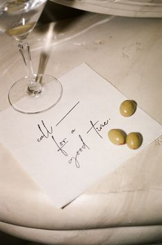 a piece of paper with two olives on it next to a glass of wine