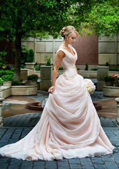 a woman in a wedding dress is standing on a brick walkway with trees and potted plants behind her