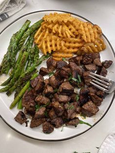 a white plate topped with meat and waffles next to asparagus