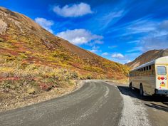 a bus is driving down the road in front of a mountain range with colorful foliage