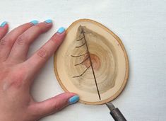 a woman's hand with blue nail polish holding a wood slice that has a tree branch on it